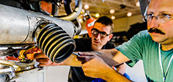Instructor adjusts a bolt on exposed machinery as student watches