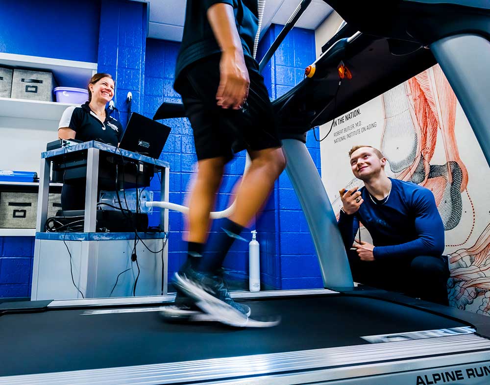 Student running on a treadmill while a fitness leader times them