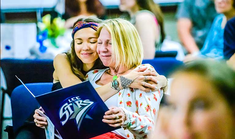 early college student hugging her mother during graduation