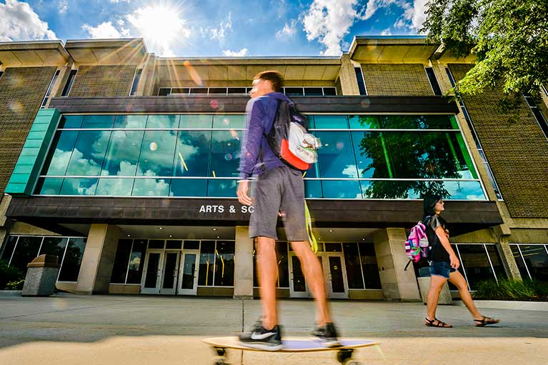 a student riding their longboard in front of the arts and sciences building