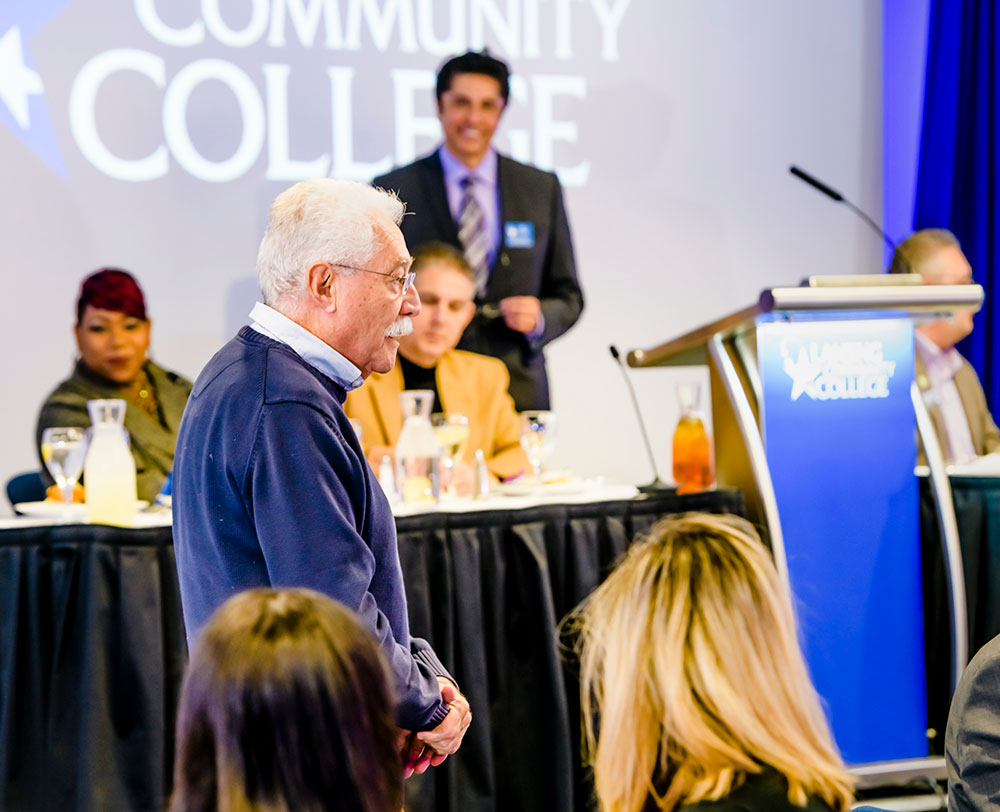 man standing to ovation and speaking to people at a luncheon