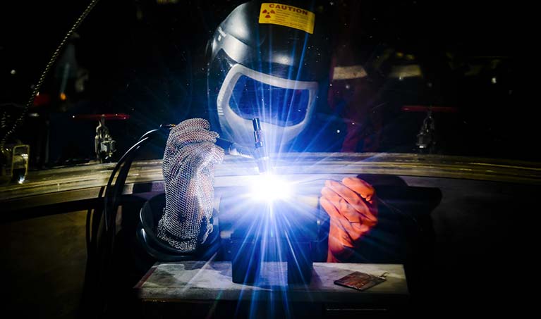 a student works on a welding project while wearing proper protection; sparks fly