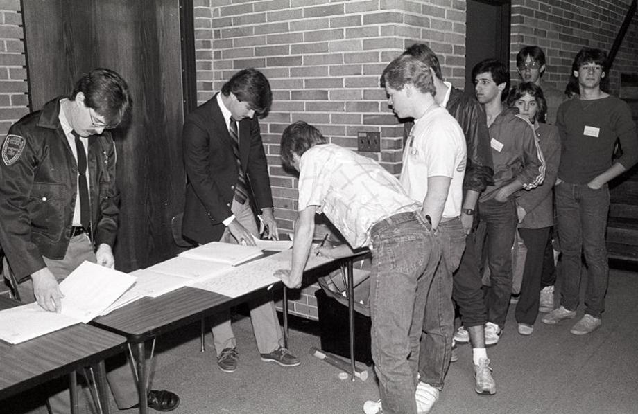 Students in line to sign a sheet of paper on a table outside a meeting room.