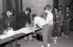 Students in line to sign a sheet of paper on a table outside a meeting room.