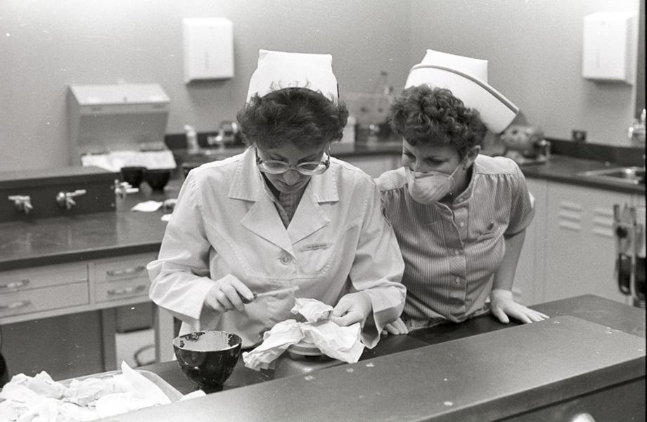 A woman pours a dental impression in a mould while another woman oversees her work.