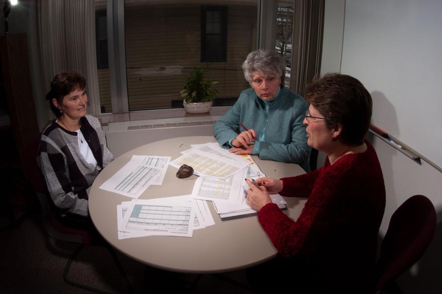 Three women from the Business & Finance Office meet around a table in an office.