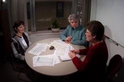 Three women from the Business & Finance Office meet around a table in an office.