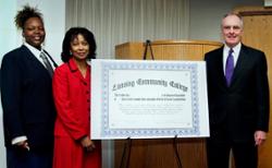 Three people stand around an oversized certificate on an easel.