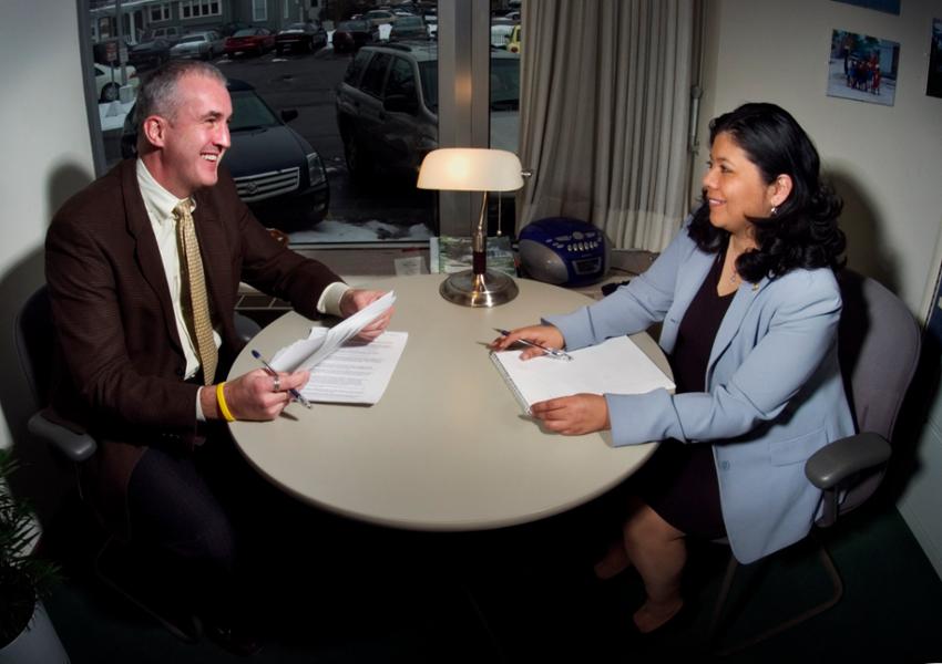 Two Human Resources employees sit across a table from each other in an office in the HR department.