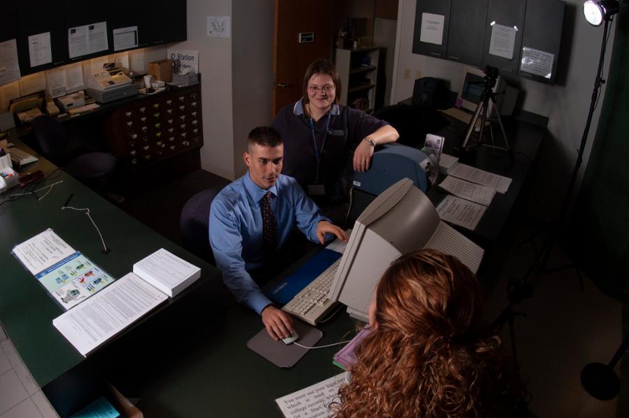 Two staff members are behind the counter to provide assistance to someone standing at the counter in the Parking & ID Services Department.