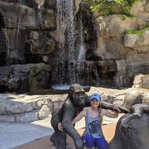 A photo of Kirbay sitting in front of a waterfall, next to a bronze statue of an ape. 