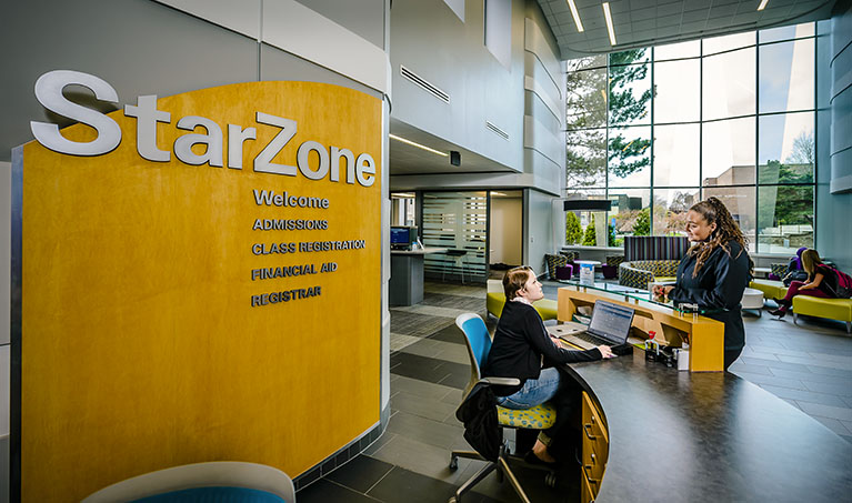 an employee sits at the starzone desk and talks with a student
