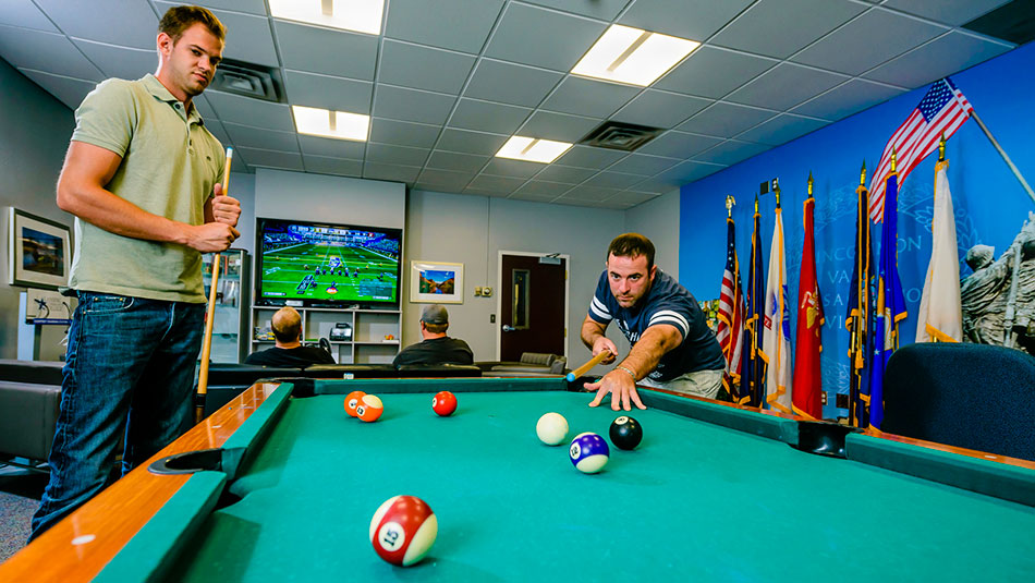 two Veteran Resource Center employees playing pool while two veteran students play madden on a tv screen in the background